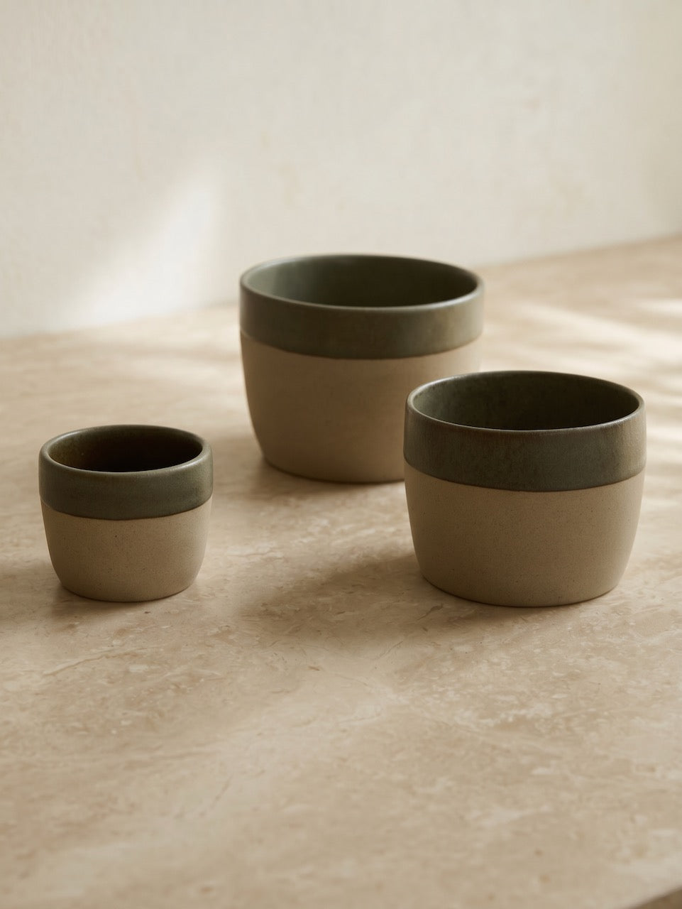 Three ceramic coffee cups with green and beige design on a marble surface