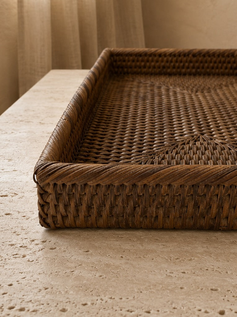 Close-up detail of a small antique brown rattan tray showcasing the rich woven texture, raised edge and handcrafted finish on a travertine tabletop.