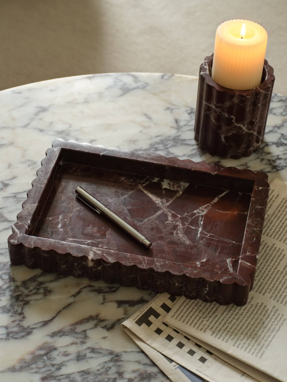 A burgundy marble ribbed tray on a marble surface with a candle and a pen placed on top of it.