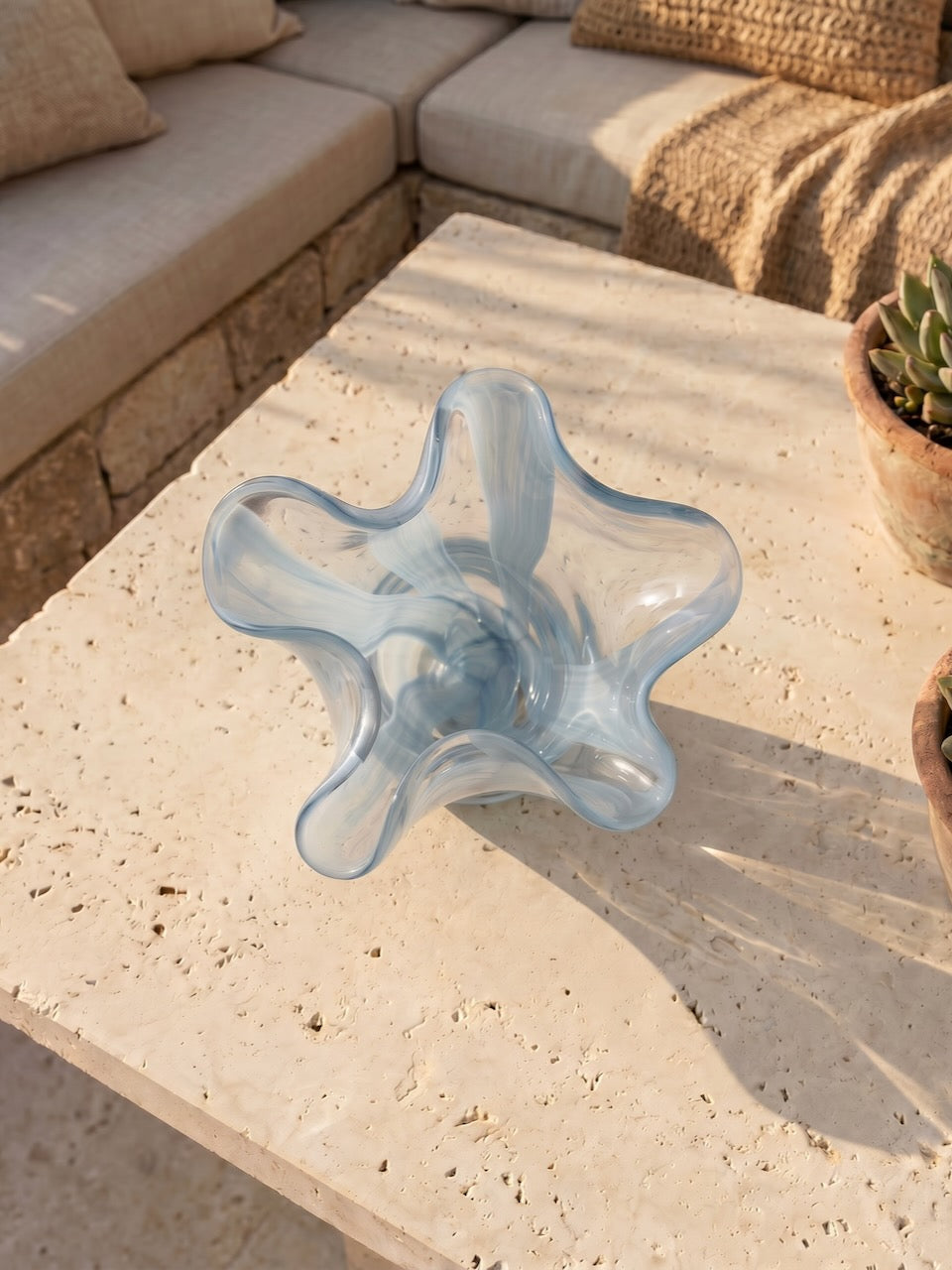 Blue glass vase on a stone surface with outdoor furniture in the background