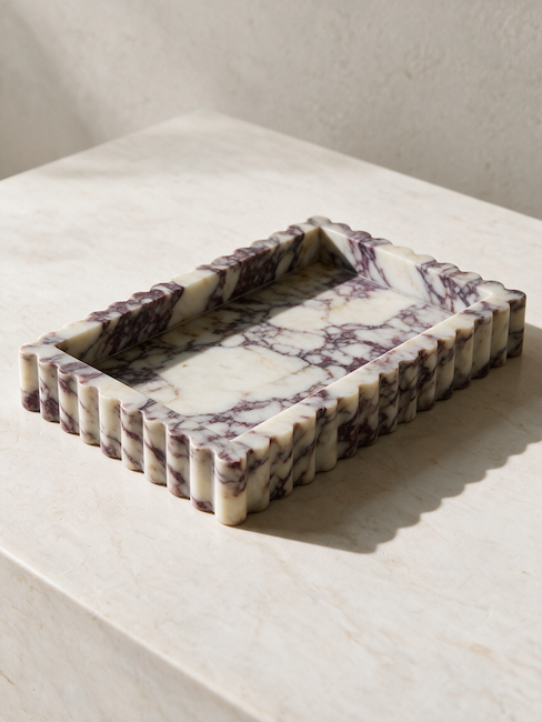A rectangular marble tray with a scalloped edge, featuring a white and purple veined pattern, resting on a light marble surface.