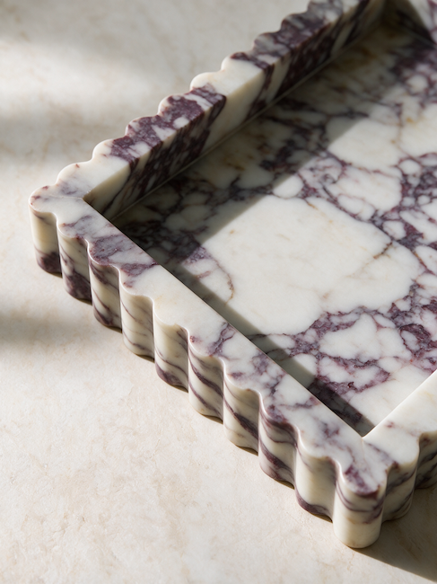 A rectangular marble tray with a scalloped fluted edge, featuring a white and dark purple veined pattern, photographed on a matching marble surface under natural light.