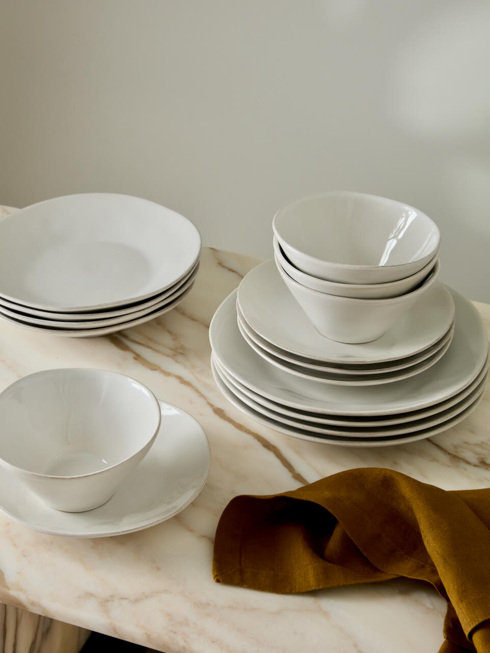 Set of white ceramic dinnerware on a marble surface with a gold napkin.
