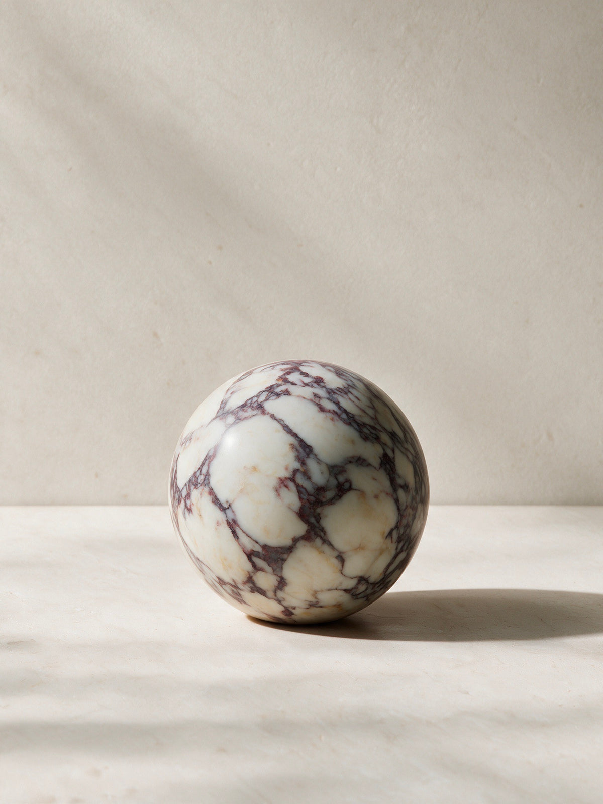 A polished spherical stone sculpture with a white base and dark brown to black veining, displayed on a light marble surface against a neutral beige background.