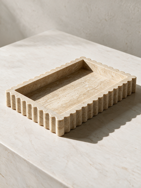 A rectangular stone tray with a scalloped fluted edge and a recessed center, shown on a light stone surface in warm natural light.