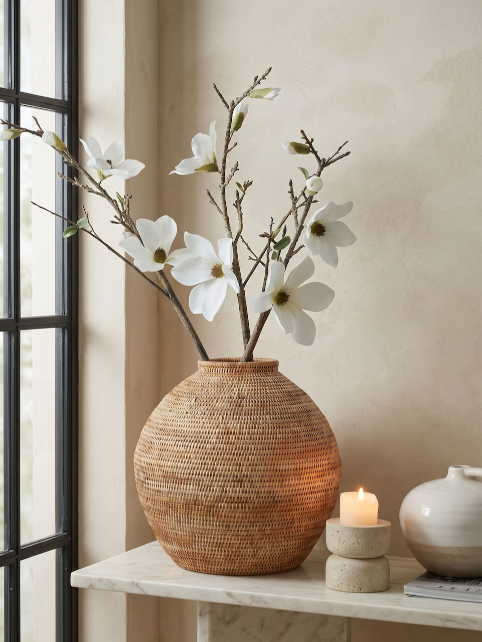 Woven vase with white flowers on a marble surface next to a candle