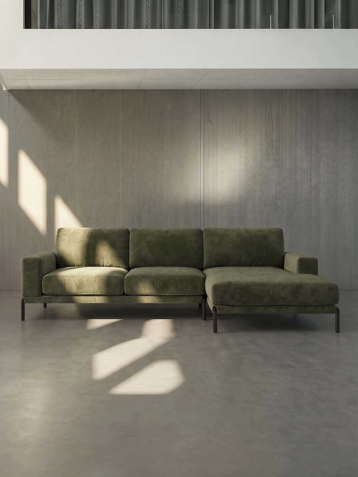 Green sectional sofa in a minimalistic room with concrete floor and gray walls.